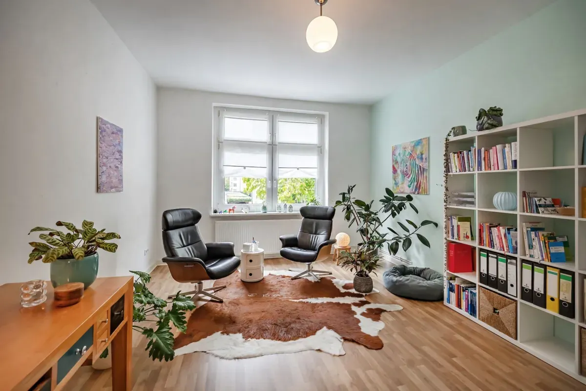Beratungsraum der Praxis in Braunschweig: zwei Ledersessel vor dem Fenster, Kuhfell auf Parkett, Bücherregal und Pflanzen